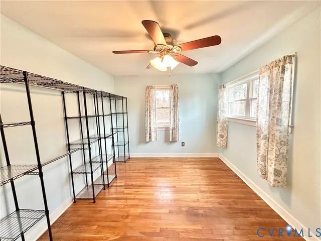 an empty room with wooden floor fan and windows