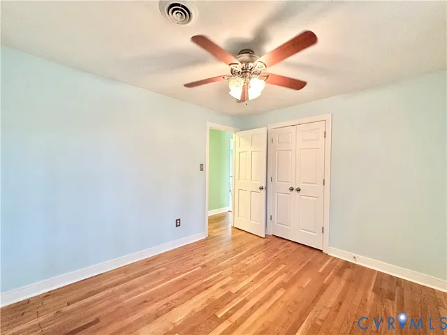 an empty room with wooden floor fan and windows