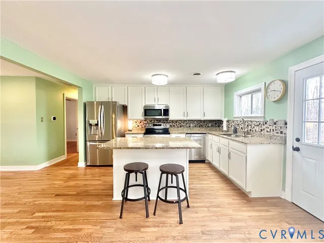 a kitchen with stainless steel appliances granite countertop a refrigerator a stove a sink and white cabinets with wooden floor