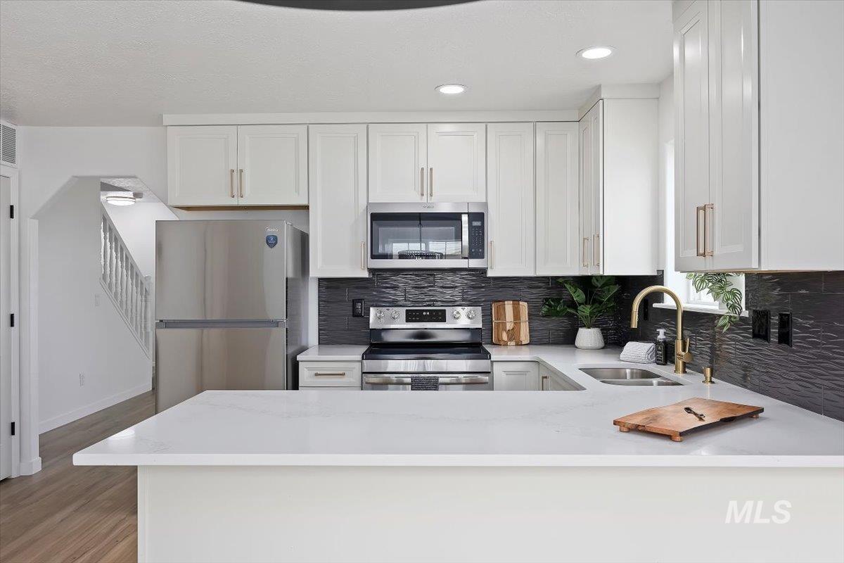 1897 Hampton Way Twin Falls, ID 83301 - Photo 8 of 48 Kitchen with stainless steel appliances, light stone countertops, white cabinetry, decorative backsplash, and light wood-type flooring