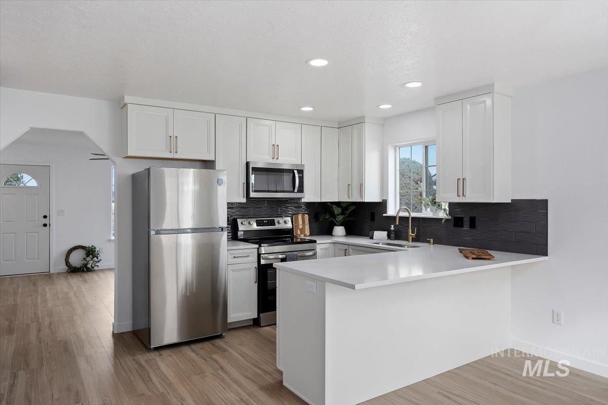 1897 Hampton Way Twin Falls, ID 83301 - Photo 9 of 48 Kitchen with stainless steel appliances, a peninsula, white cabinets, backsplash, and light wood-type flooring