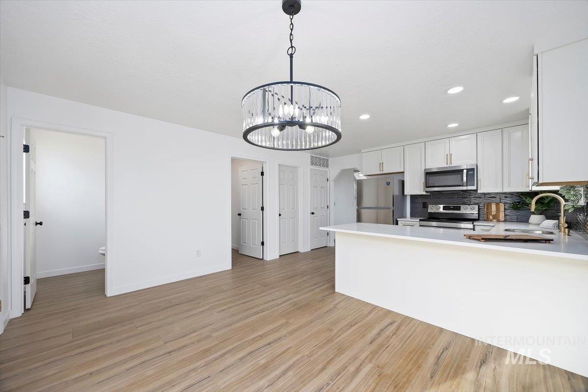 1897 Hampton Way Twin Falls, ID 83301 - Photo 10 of 48 Kitchen with suspended lighting, stainless steel appliances, tasteful backsplash, light wood finished floors, and white cabinets
