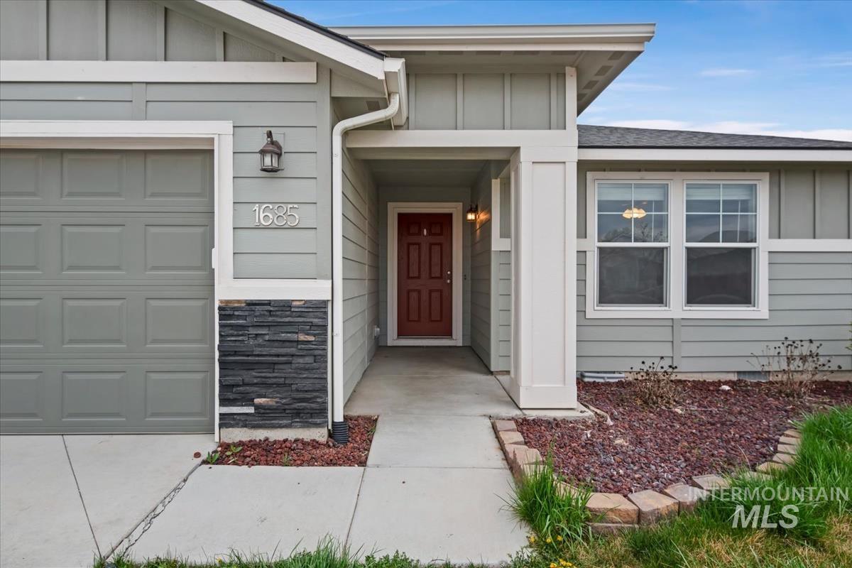Property entrance featuring board and batten siding, an attached garage, stone siding, and a shingled roof