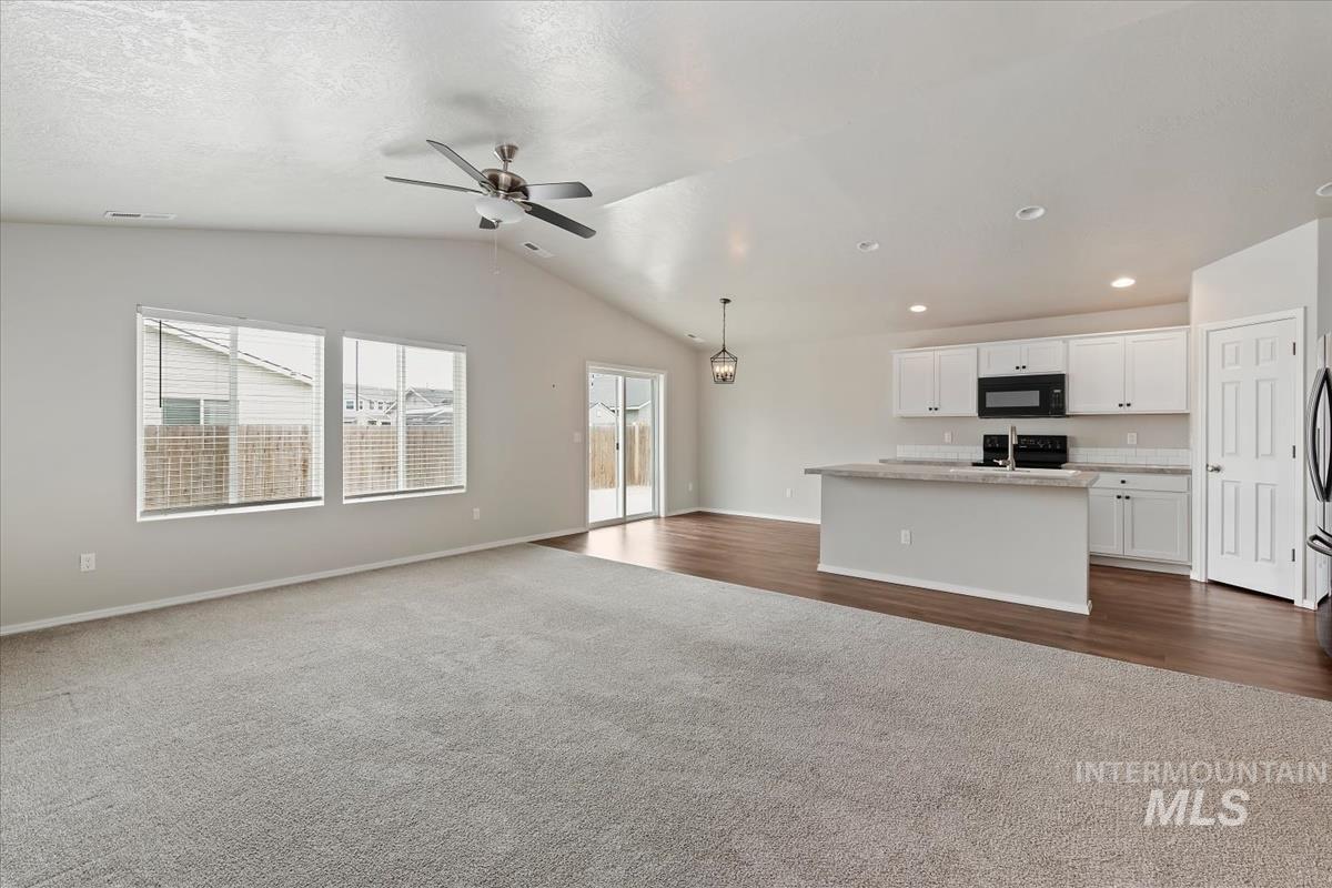 1685 Southwest Levant Way Mountain Home, ID 83647 - Photo 12 of 31 Unfurnished living room featuring dark colored carpet, vaulted ceiling, and ceiling fan