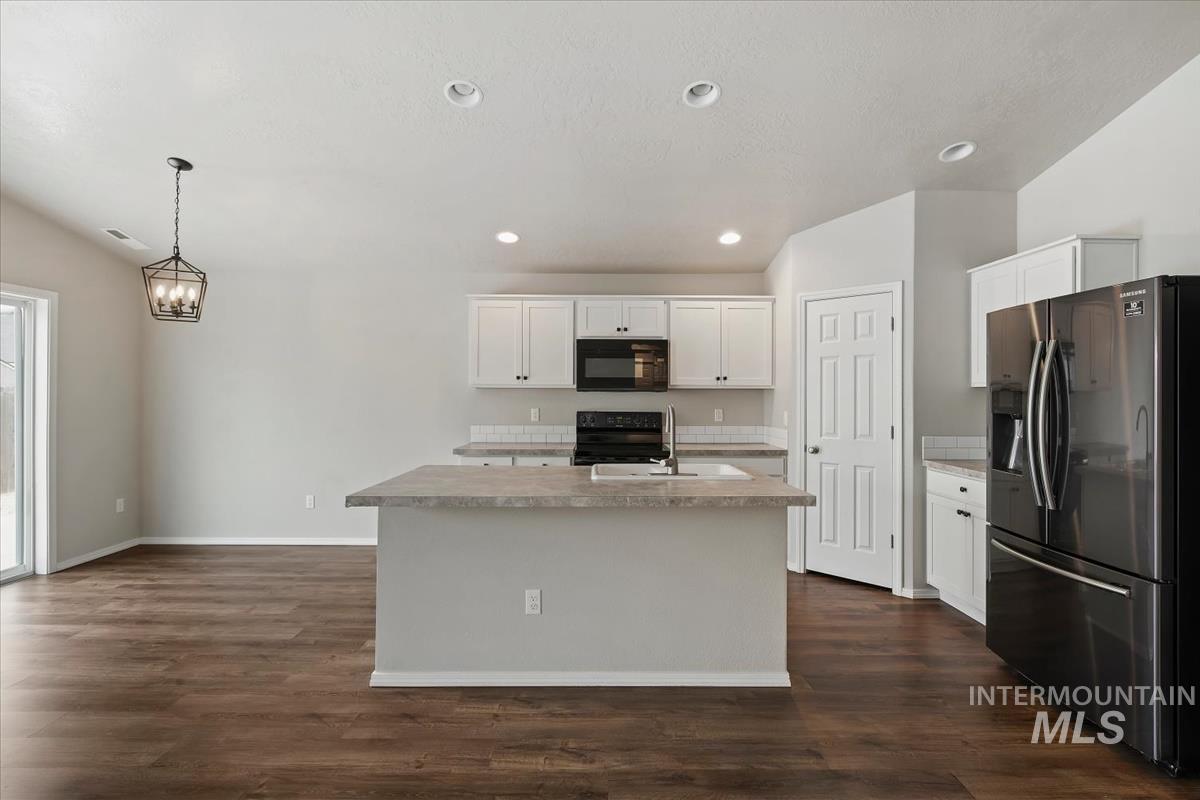1685 Southwest Levant Way Mountain Home, ID 83647 - Photo 9 of 31 Kitchen featuring black appliances, vaulted ceiling, white cabinetry, dark wood-type flooring, and pendant lighting