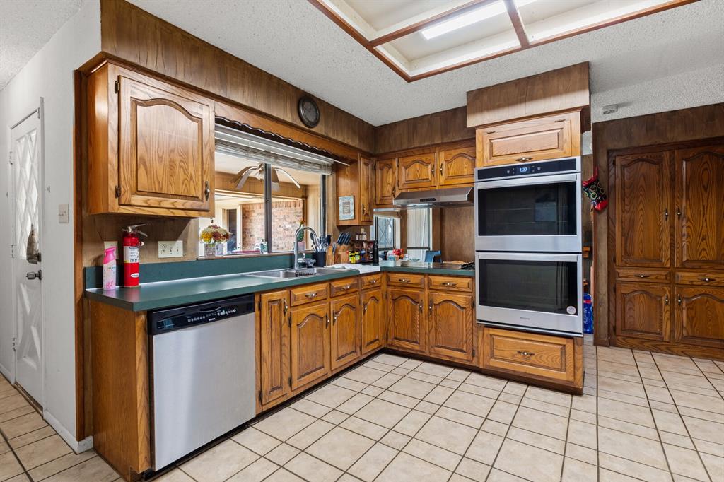 1502 Hinchliffe Road Mexia, TX 76667 - Photo 22 of 40 Kitchen with brown cabinetry, under cabinet range hood, a textured ceiling, and appliances with stainless steel finishes