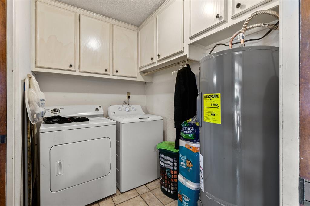 1502 Hinchliffe Road Mexia, TX 76667 - Photo 25 of 40 Laundry room with electric water heater, a textured ceiling, light tile patterned floors, washer and dryer, and cabinet space