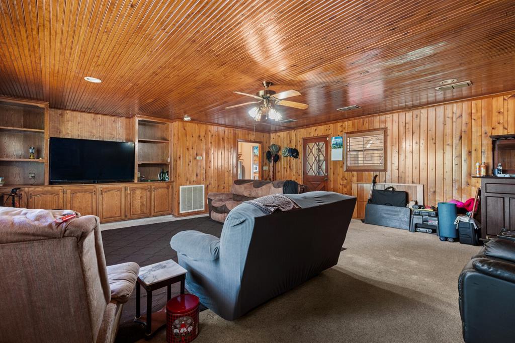 1502 Hinchliffe Road Mexia, TX 76667 - Photo 28 of 40 Living area featuring wooden walls, ceiling fan, dark colored carpet, and visible vents