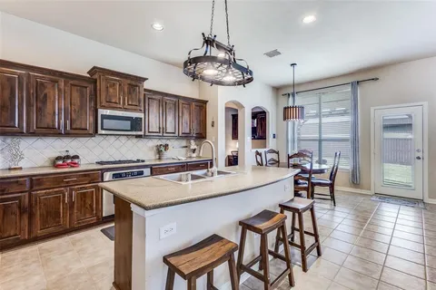 a kitchen with stainless steel appliances granite countertop a stove top oven a sink a dining table and chairs with wooden floor