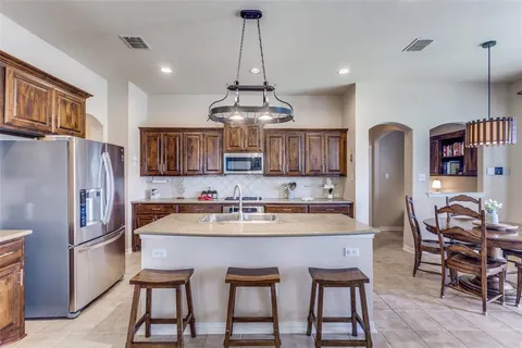 a kitchen with stainless steel appliances granite countertop a dining table and chairs a refrigerator with wooden floors