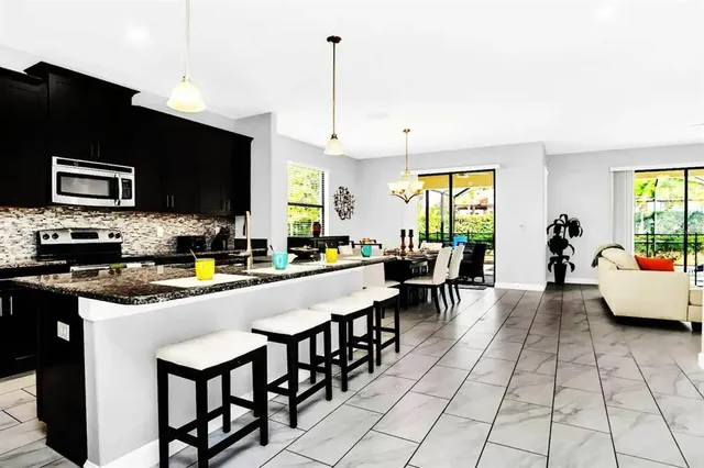 a kitchen with stainless steel appliances granite countertop a stove top oven a sink a dining table and chairs with the wooden floor