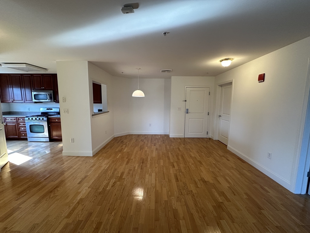 318 Rindge Avenue, Unit 216 Cambridge, MA 02140 - Photo 1 of 15 an empty room with kitchen view and wooden floor