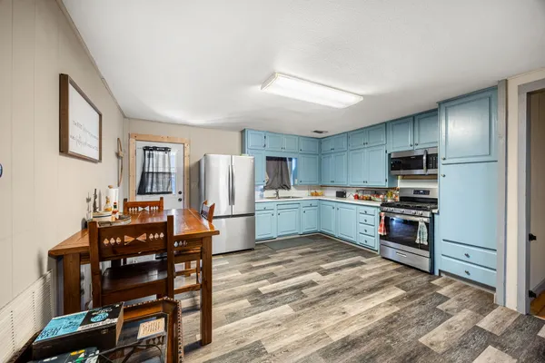 a kitchen with stainless steel appliances a stove a sink dishwasher a refrigerator with a dining table and chairs