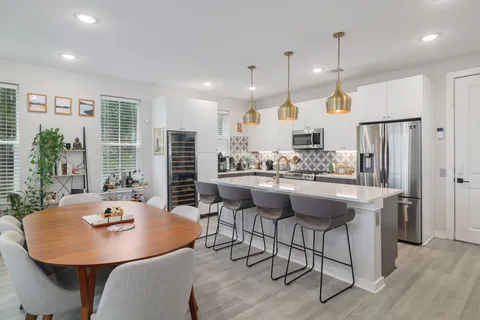 a kitchen with stainless steel appliances kitchen island granite countertop a dining table chairs and a refrigerator