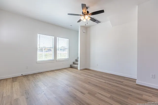 an empty room with wooden floor fan and windows