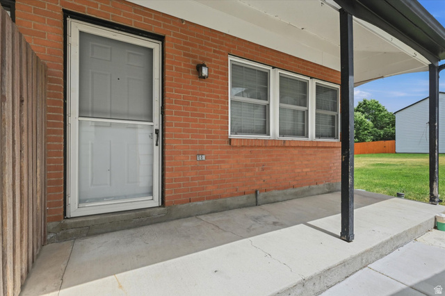 187 West 1190th Street North Logan, UT 84341 - Photo 10 of 12 Brick exterior featuring a covered concrete patio, a white entry door with an exterior screen door, and multiple windows with blinds