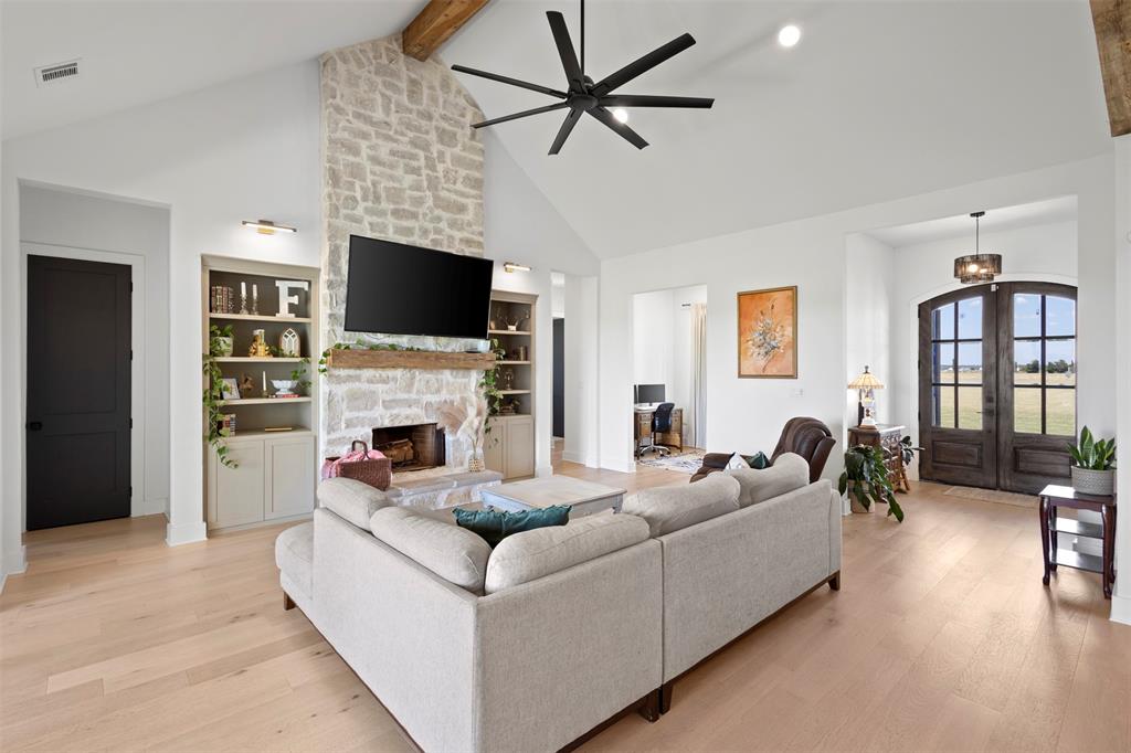 861 Brindley Road Maypearl, TX 76064 - Photo 6 of 36 Vaulted ceiling with exposed wood beam, stone fireplace with wood mantel, built-in shelving, wood-finish flooring, and arched double entry doors