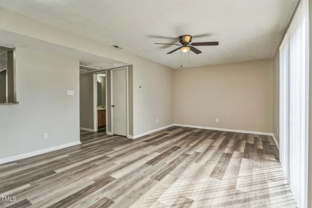 a view of an empty room with wooden floor and a ceiling fan
