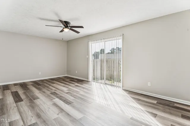an empty room with wooden floor fan and windows