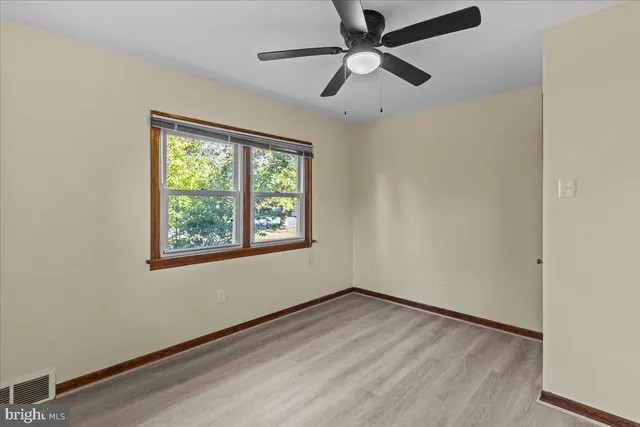 an empty room with wooden floor ceiling fan and windows