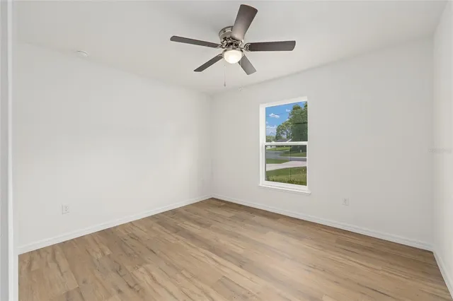an empty room with wooden floor ceiling fan and windows