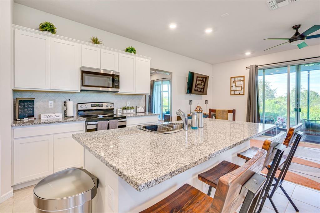 5443 Elmview Crossing Wesley Chapel, FL 33545 - Photo 8 of 41 a kitchen with stainless steel appliances granite countertop a sink dishwasher a stove a refrigerator a microwave oven with white cabinets and wooden floor