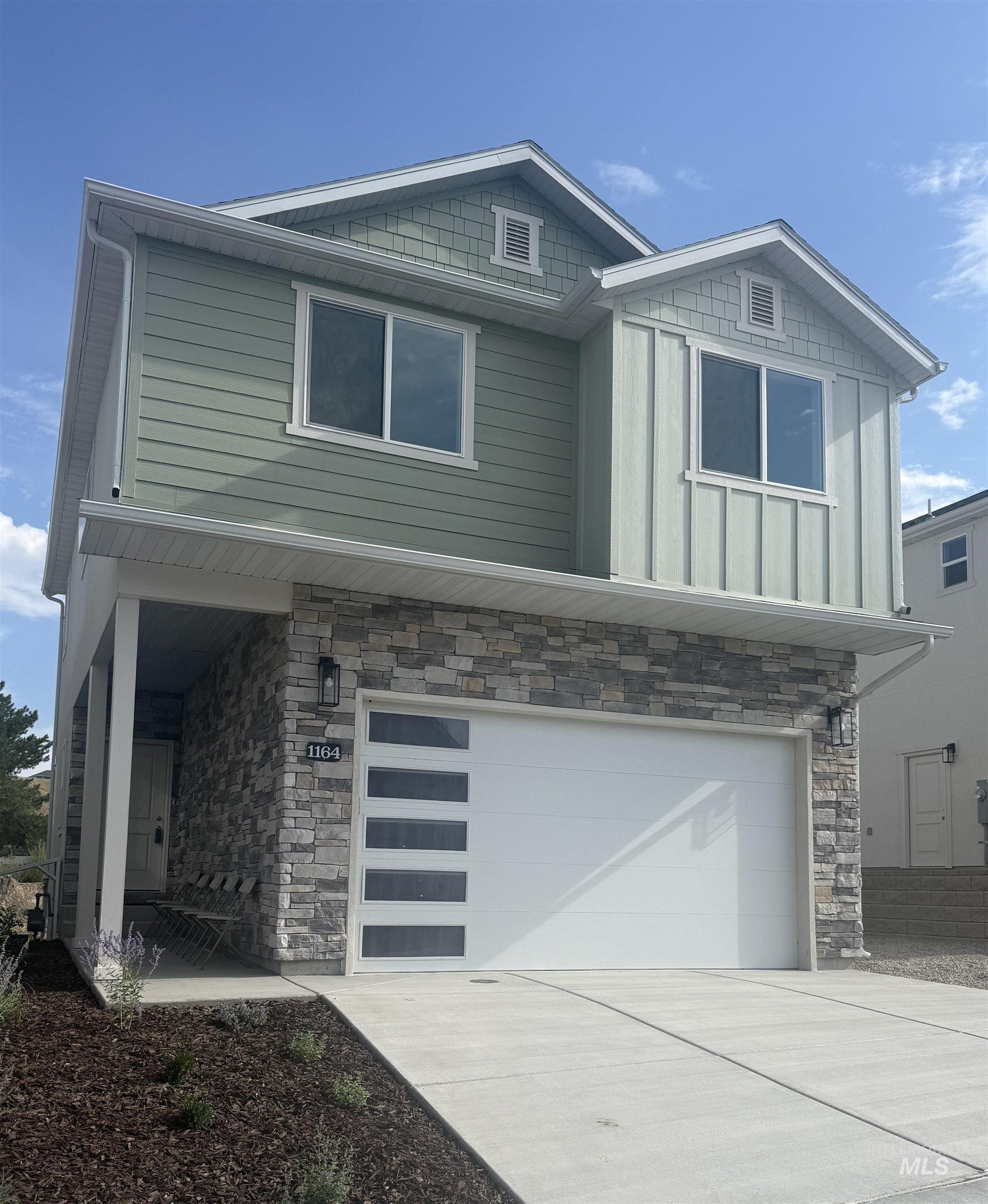 Craftsman house with stone siding, a garage, driveway, and board and batten siding