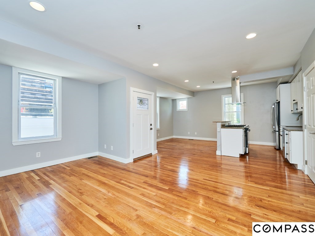 145 Pearl Street, Unit 145 Cambridge, MA 02139 - Photo 7 of 26 a view of an empty room with wooden floor and a kitchen
