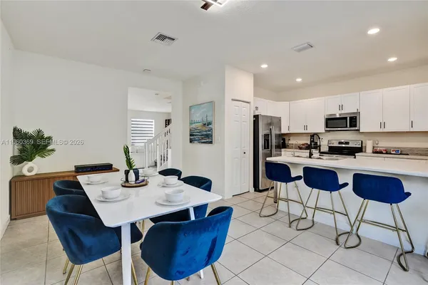 a kitchen with stainless steel appliances kitchen island granite countertop a dining table chairs and a refrigerator