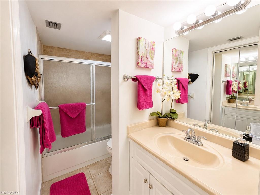 600 Neapolitan Way, Unit 449 Naples, FL 34103 - Photo 15 of 44 Bathroom featuring a single vanity with integrated sink, white cabinetry, and a full-width mirror with overhead lighting