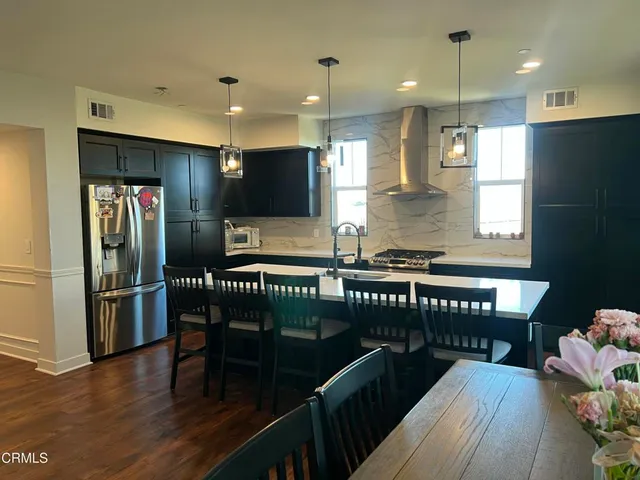 a kitchen with stainless steel appliances kitchen island granite countertop a refrigerator a stove and a dining table with wooden floor