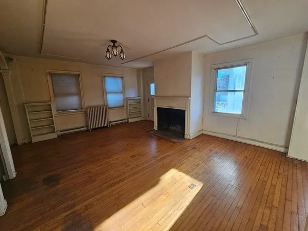 a view of an empty room with wooden floor fireplace and a window