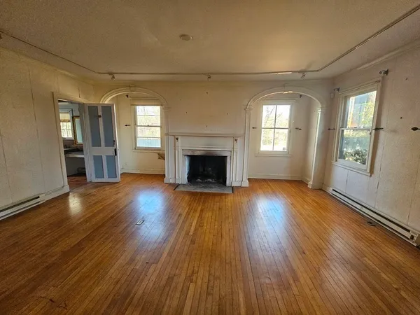an empty room with wooden floor fireplace and windows