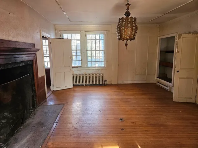 an empty room with wooden floor fireplace and windows