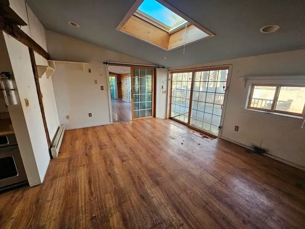 a view of an empty room with wooden floor and a window