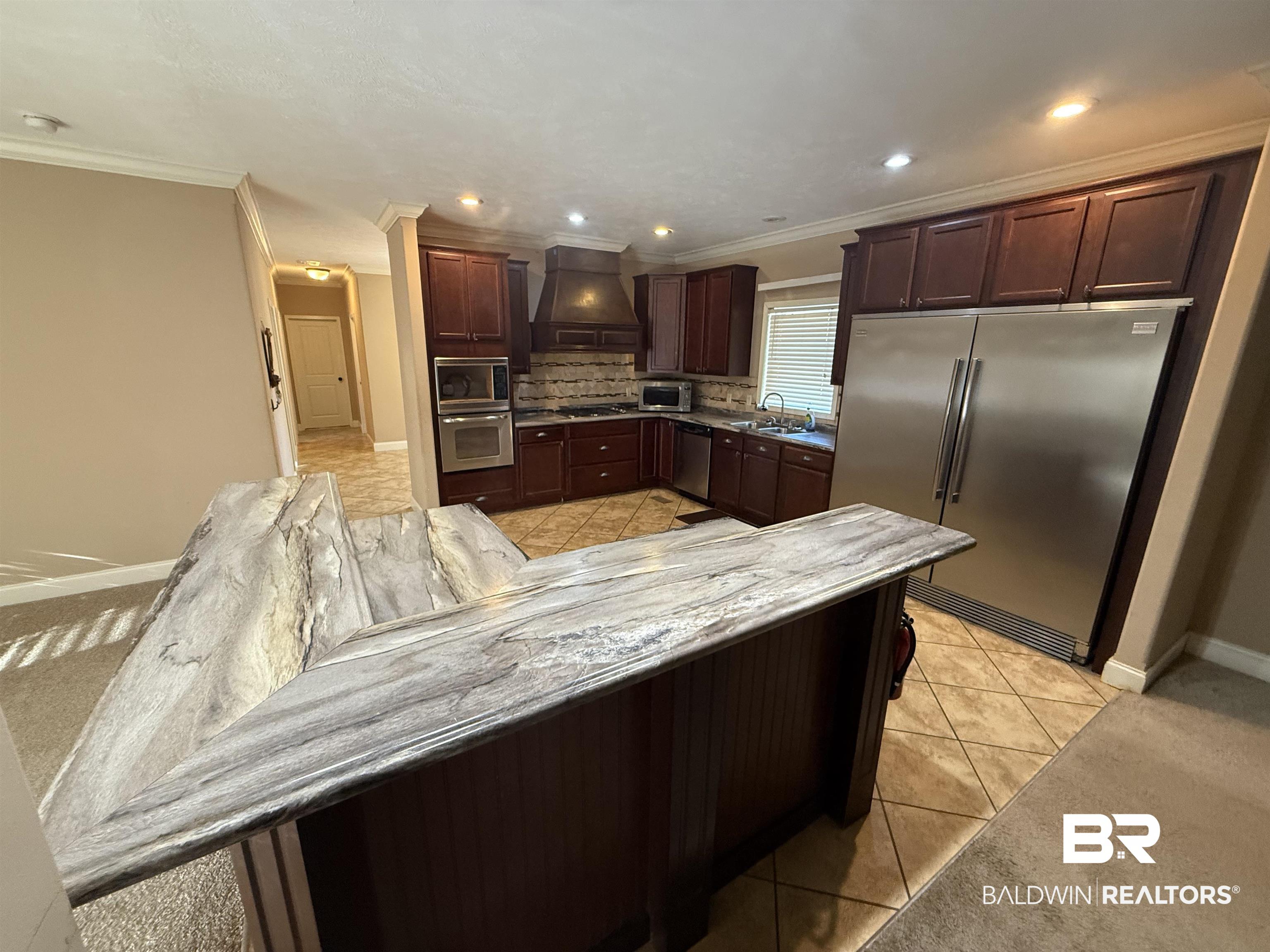1274 Caney Loop Lillian, AL 36549 - Photo 8 of 19 Kitchen featuring stainless steel appliances, light tile patterned floors, dark wood finish cabinets, crown molding, and decorative backsplash