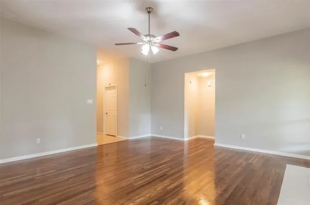 a view of an empty room with wooden floor and a ceiling fan