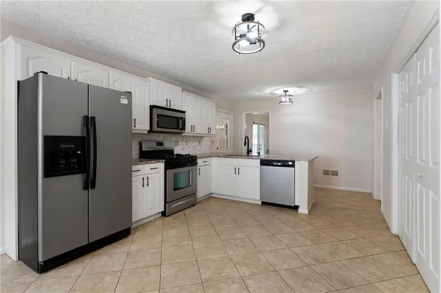a large white kitchen with stainless steel appliances granite countertop a refrigerator and a sink