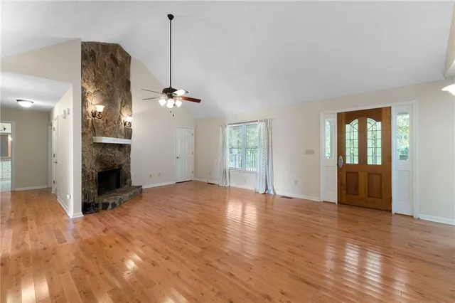 a view of an empty room with wooden floor fireplace and a window