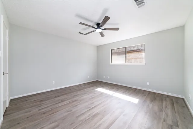 an empty room with wooden floor fan and windows