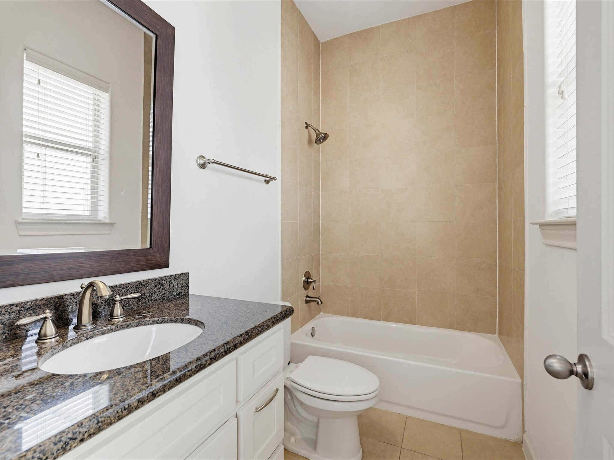 9427 London Bridge Station Houston, TX 77045 - Photo 20 of 30 This bathroom features a sleek granite countertop with dual faucets, a large mirror, and a bathtub with a tiled wall. Natural light streams through the window, creating a bright and inviting space.