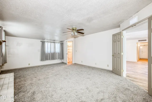 a view of an empty room with wooden floor and a kitchen