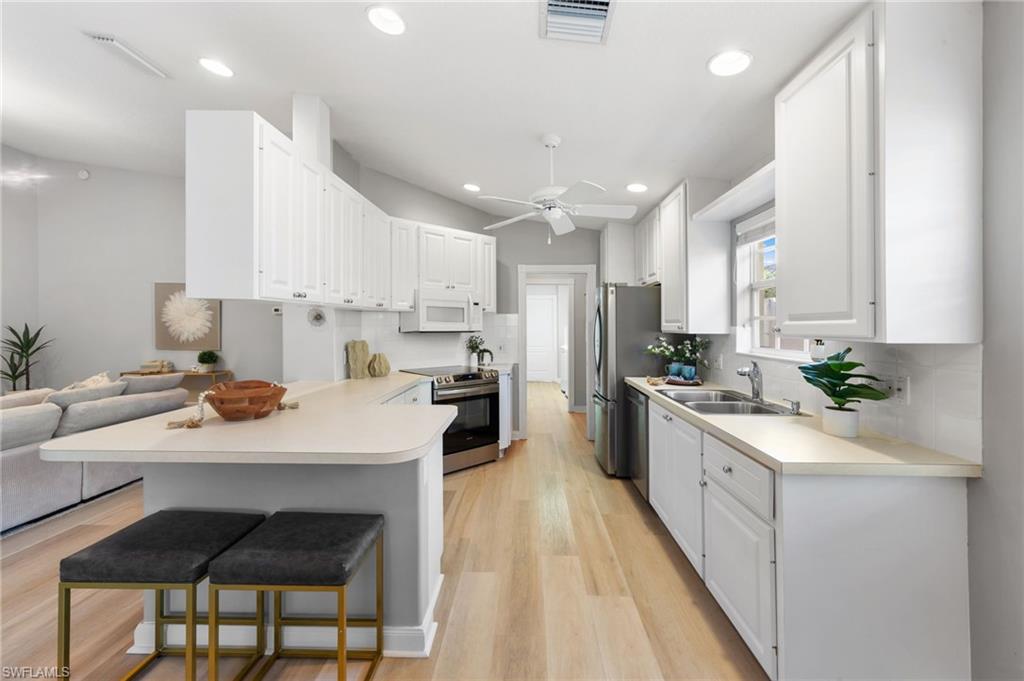 3238 Barbados Lane Naples, FL 34119 - Photo 5 of 43 a kitchen with stainless steel appliances kitchen island granite countertop a sink a stove a refrigerator and white cabinets with wooden floor