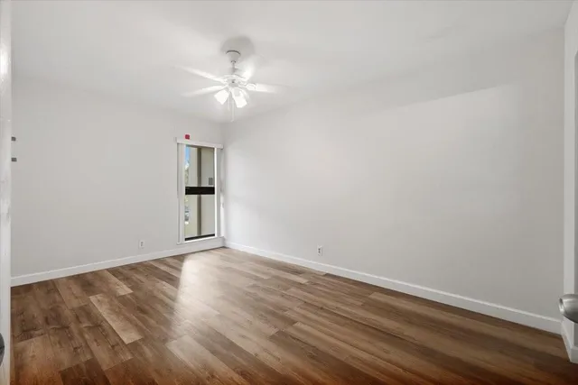 a view of an empty room with wooden floor and a ceiling fan