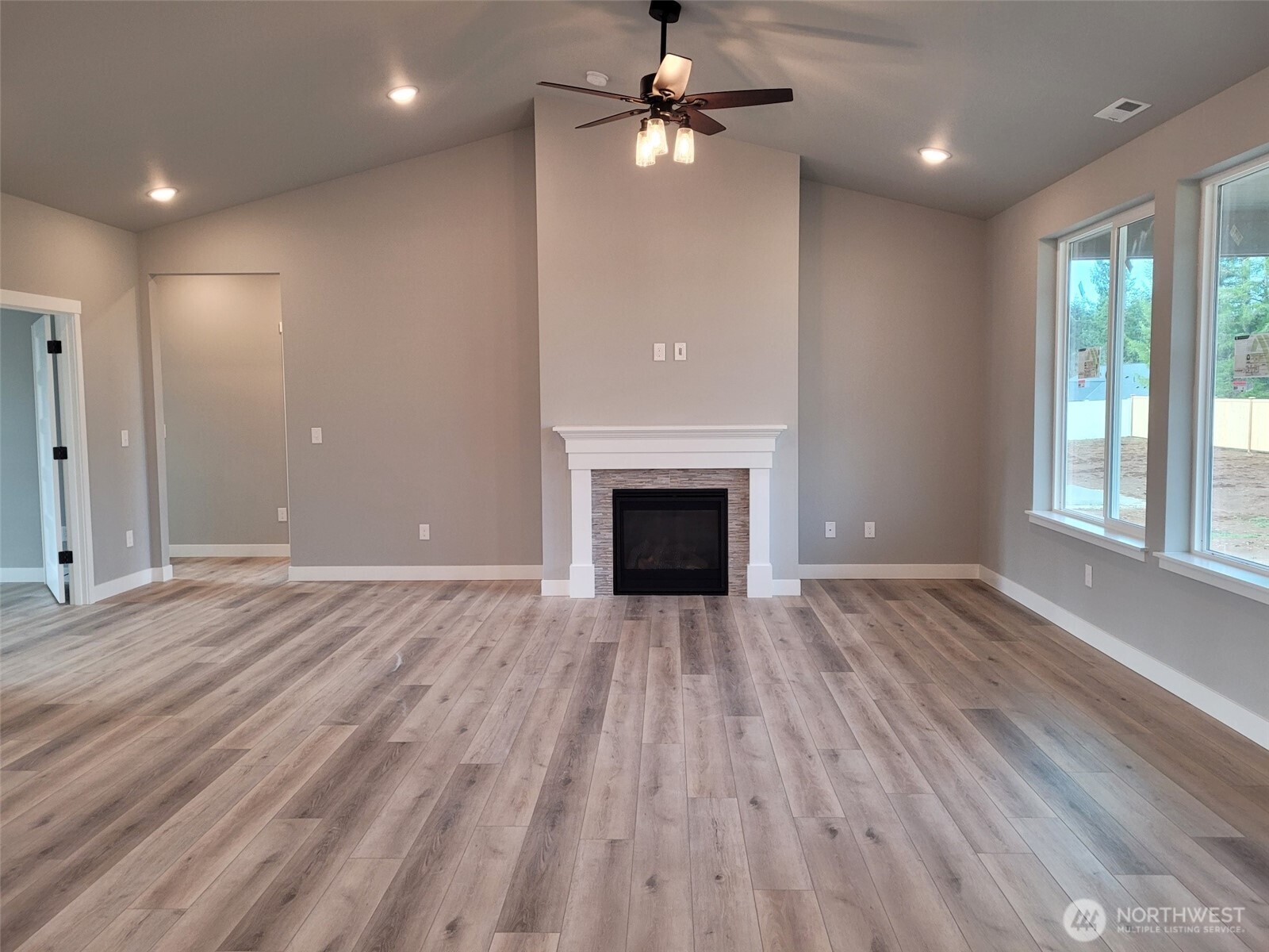 22 Raven Lane Elma, WA 98541 - Photo 10 of 21 an empty room with wooden floor a ceiling fan a fireplace and windows