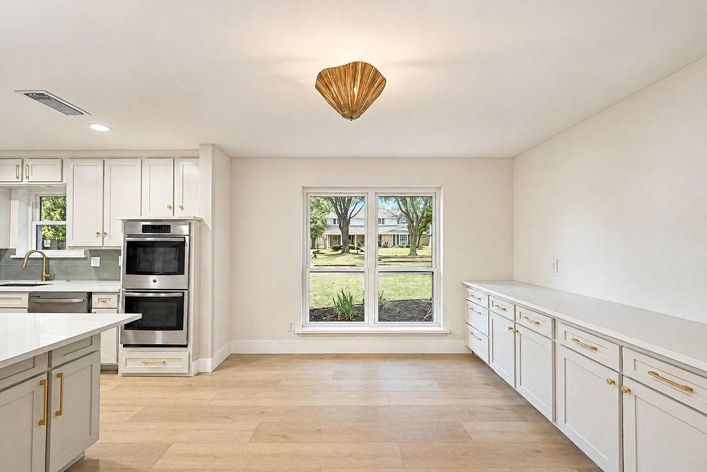 1904 Apollo Road Richardson, TX 75081 - Photo 7 of 40 White shaker cabinetry, stainless steel double wall ovens, light wood-finish flooring, and a built-in buffet with ample storage