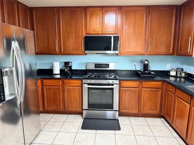 a kitchen with stainless steel appliances granite countertop a stove a sink dishwasher and a refrigerator with wooden cabinets