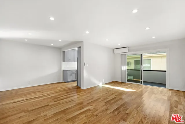 a view of an empty room with wooden floor and kitchen