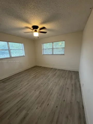 an empty room with wooden floor chandelier fan and windows