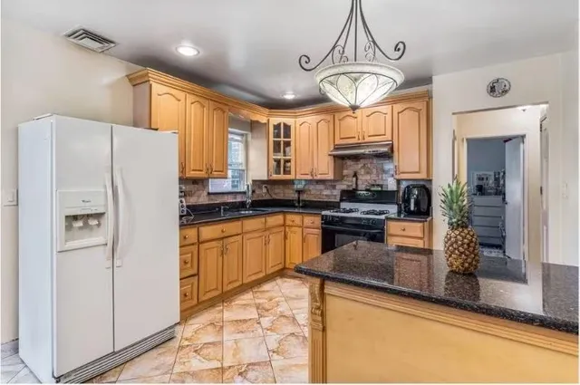 a kitchen with granite countertop a refrigerator a sink a stove a dining table and chairs